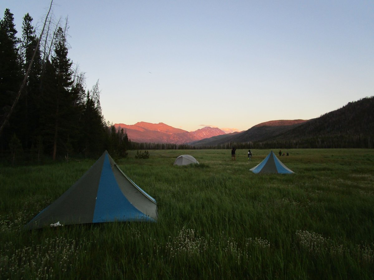 Alpenglow lights up the mountains behind tents and basecamp on a trip